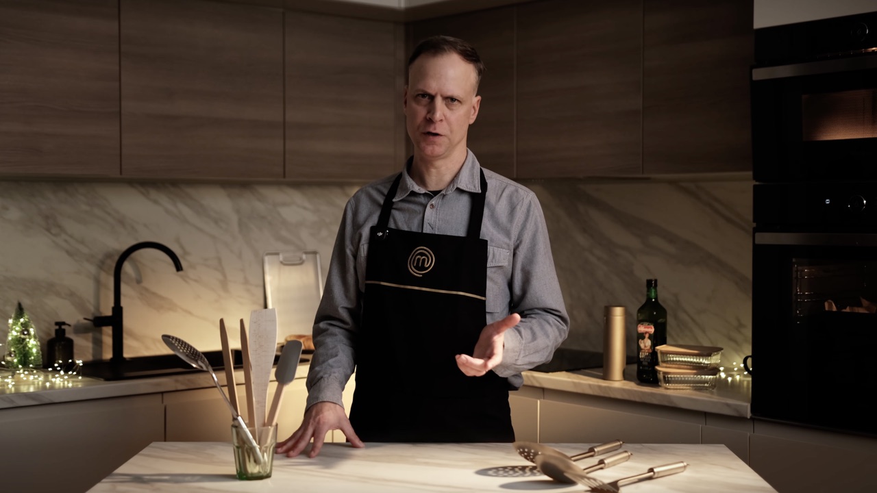 Presenter in an apron demonstrating cookware in a kitchen
